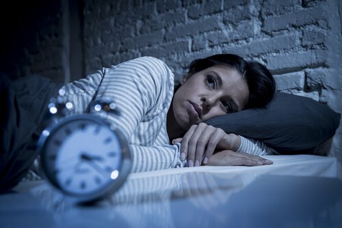 Woman lying awake at night looking at alarm clock showing insomnia